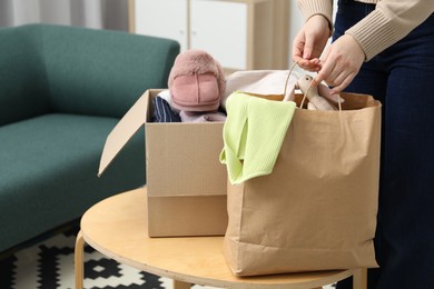 Photo of Woman with paper bag and box of used clothes at coffee table indoors, closeup