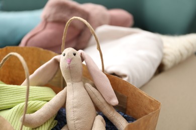 Photo of Used clothes and toy in paper bag indoors, closeup