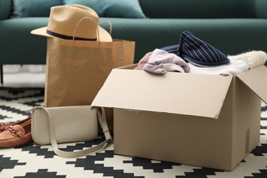 Photo of Used clothes, paper bag and box on floor indoors