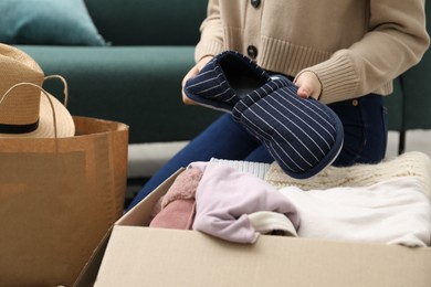 Photo of Woman putting slippers into box with used clothes indoors, closeup