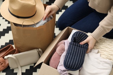 Photo of Woman putting slippers into box with used clothes indoors, closeup