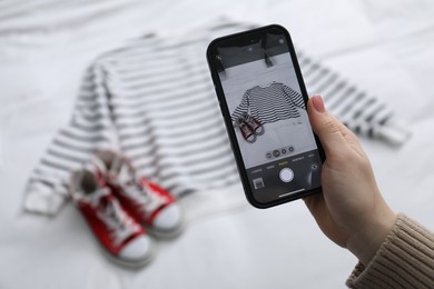 Photo of Woman with smartphone taking photo of her used clothes indoors, selective focus