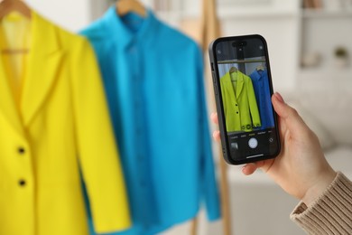 Photo of Woman with smartphone taking photo of her used clothes indoors, selective focus