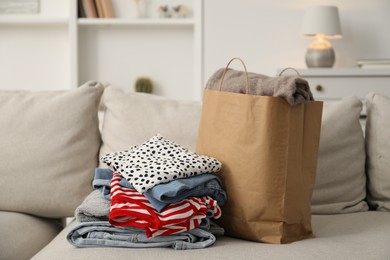 Photo of Stack of different used clothes and paper bag on sofa indoors