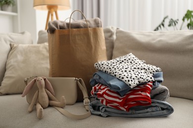 Photo of Stack of different used clothes, toy and paper bag on sofa indoors