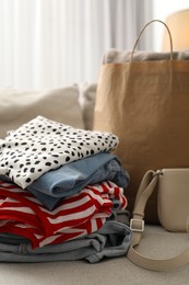 Photo of Stack of different used clothes and paper bag on sofa indoors