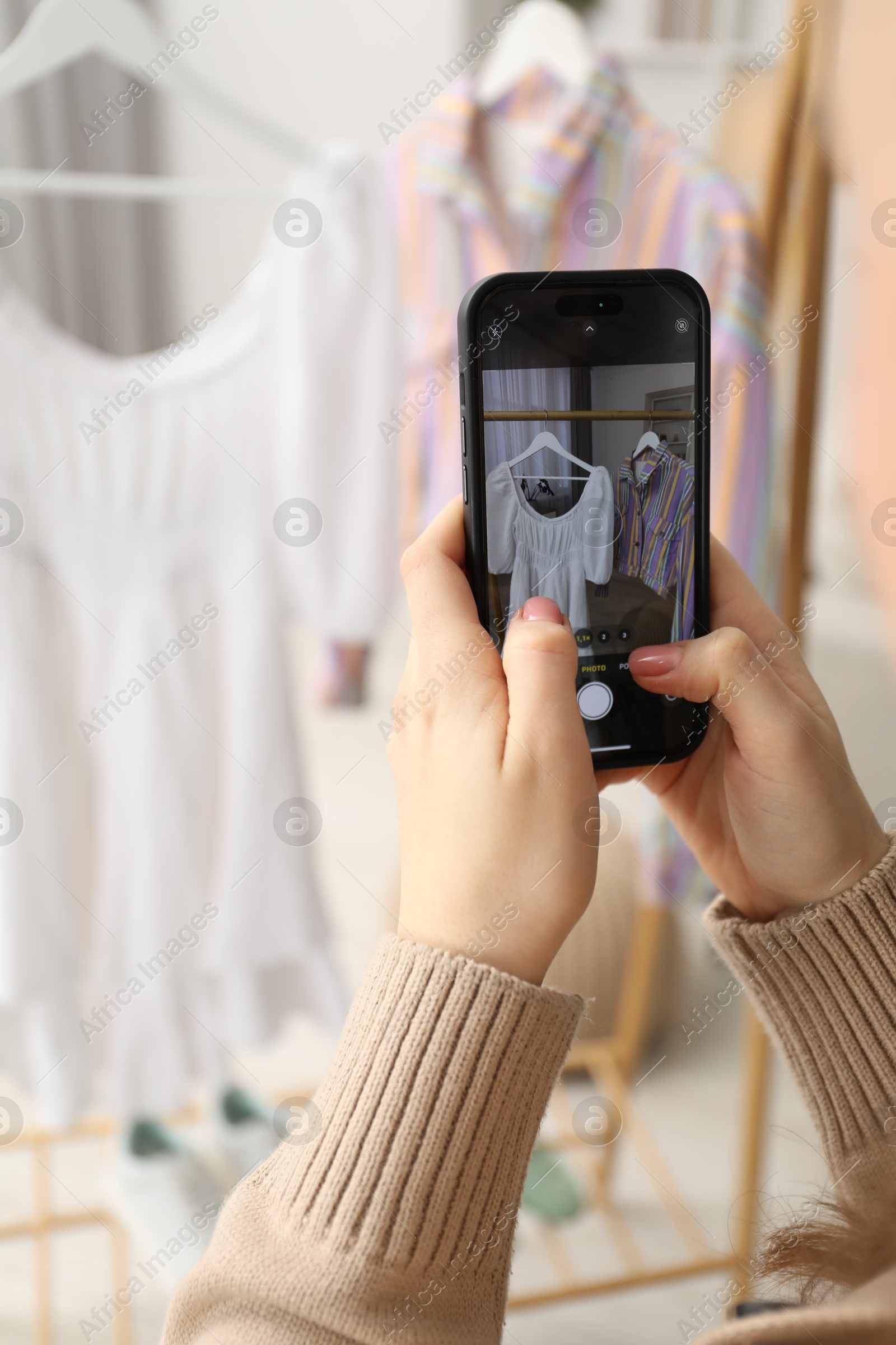 Photo of Woman with smartphone taking photo of her used clothes indoors, selective focus