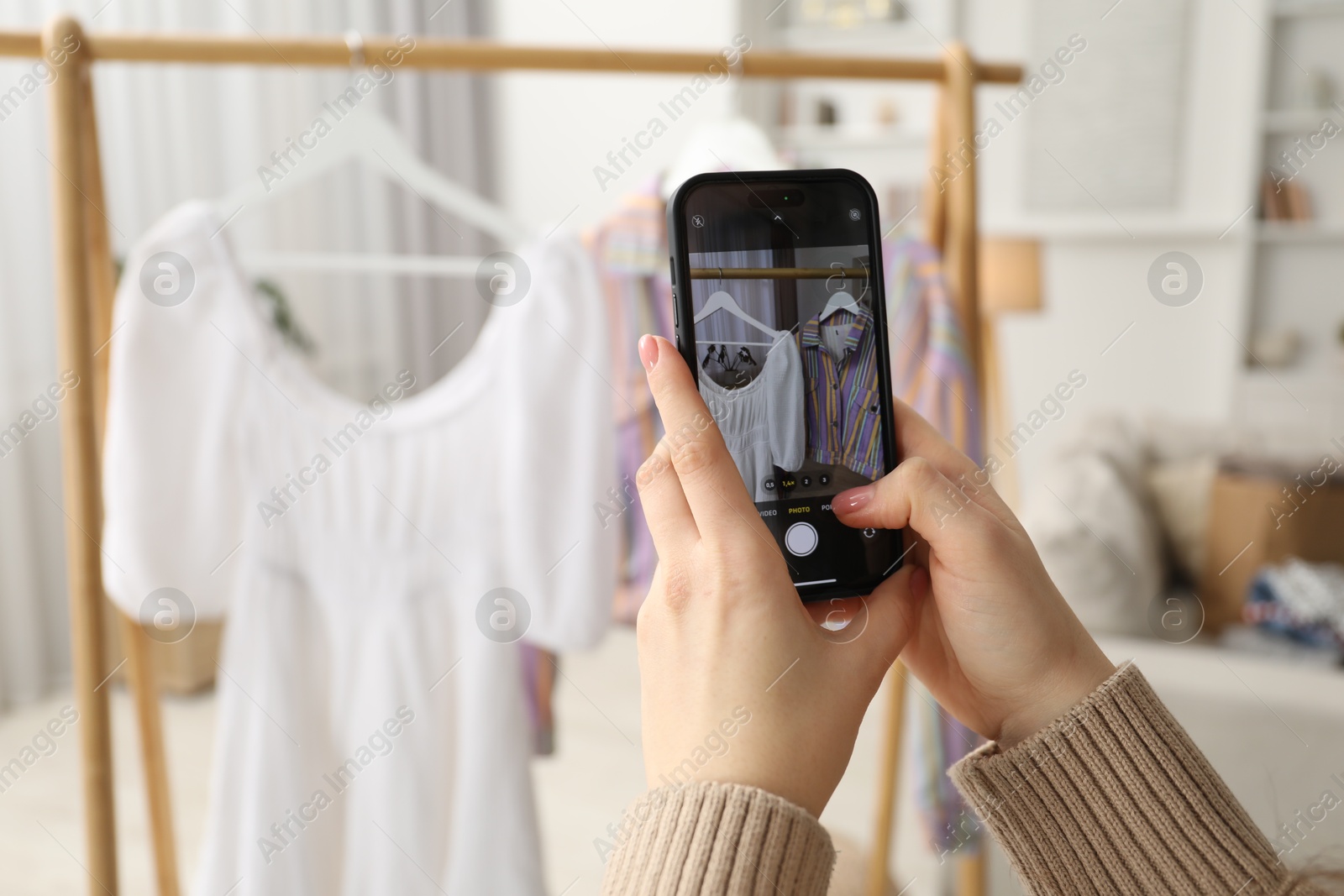 Photo of Woman with smartphone taking photo of her used clothes indoors, selective focus