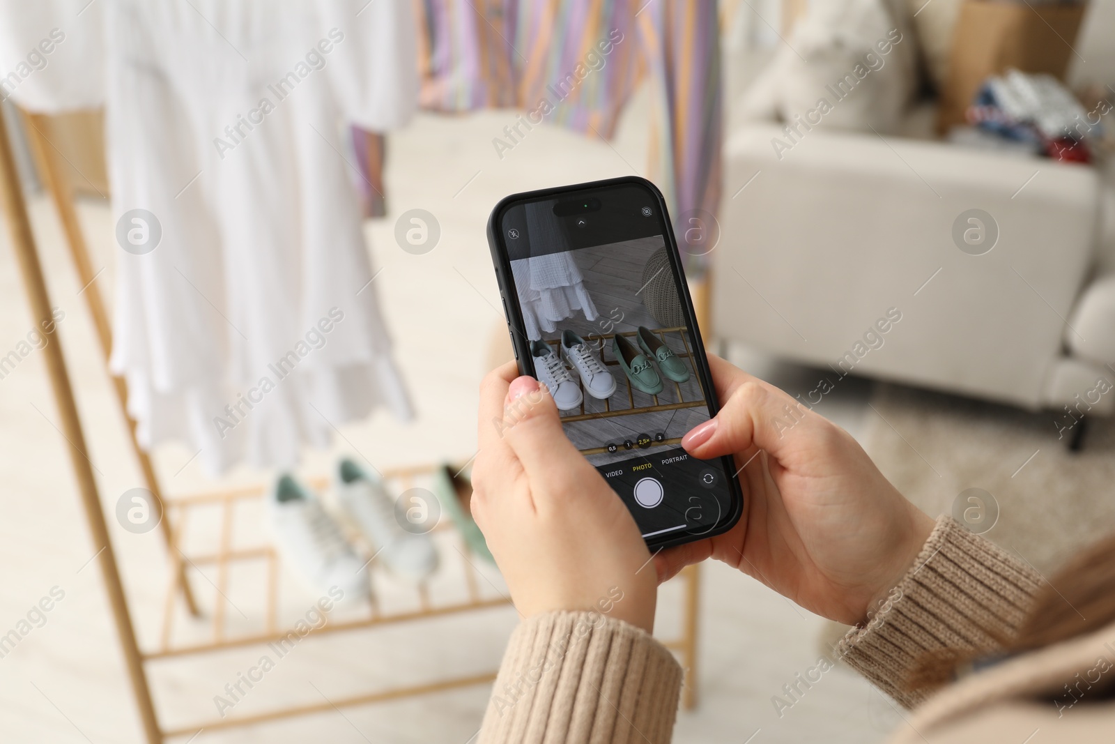 Photo of Reuse and donation of used clothes. Woman with smartphone taking photo of her shoes indoors, selective focus