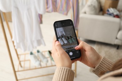 Photo of Reuse and donation of used clothes. Woman with smartphone taking photo of her shoes indoors, selective focus