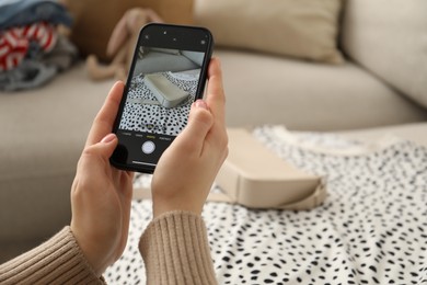 Photo of Reuse and donation of used clothes. Woman with smartphone taking photo of her bag indoors, selective focus