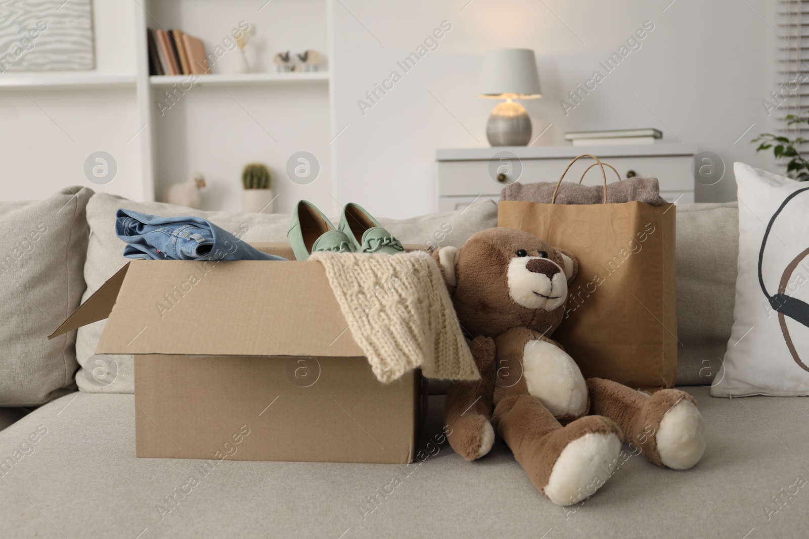 Photo of Used clothes in paper bag and box on sofa indoors