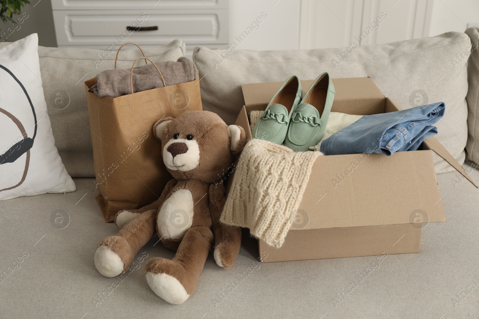 Photo of Used clothes in paper bag and box on sofa indoors