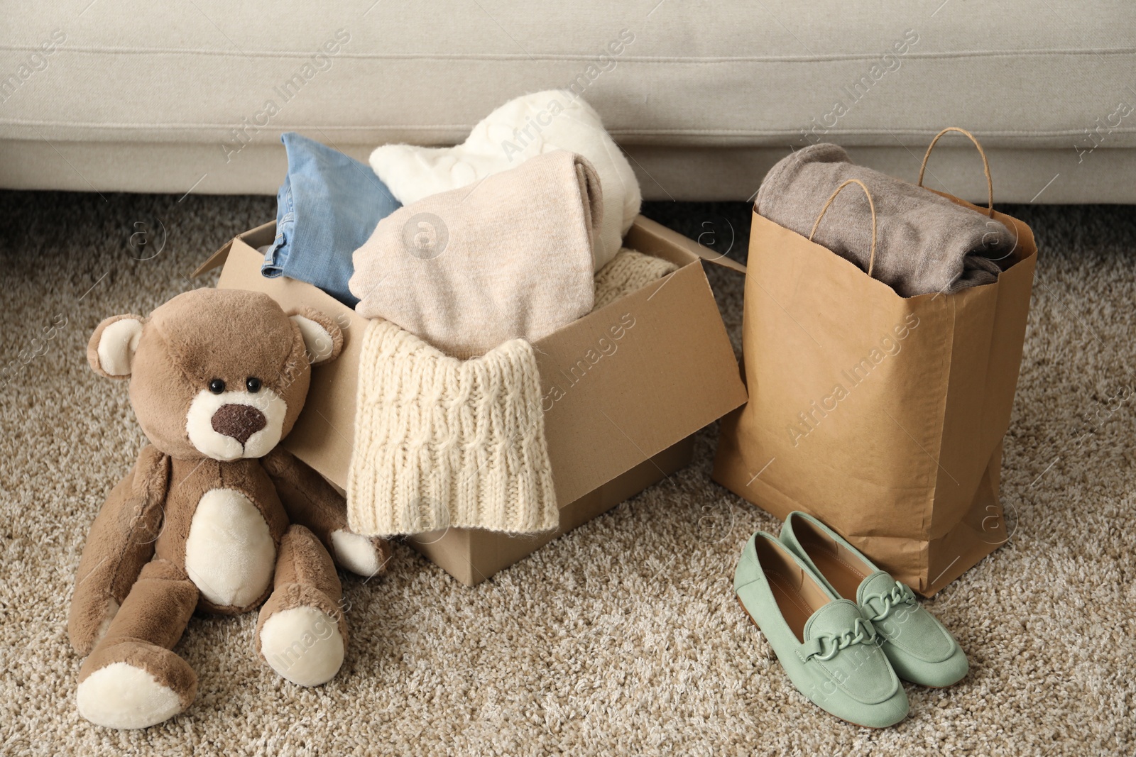 Photo of Used clothes, toy, paper bag and box on floor indoors