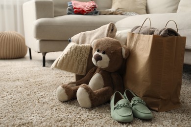 Photo of Used clothes, toy, paper bag and shoes on floor indoors, space for text