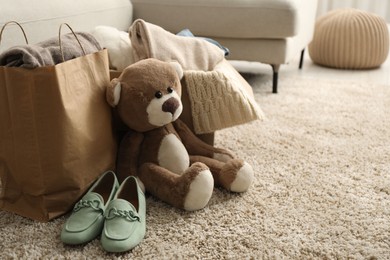 Photo of Used clothes, toy, paper bag and shoes on floor indoors, space for text