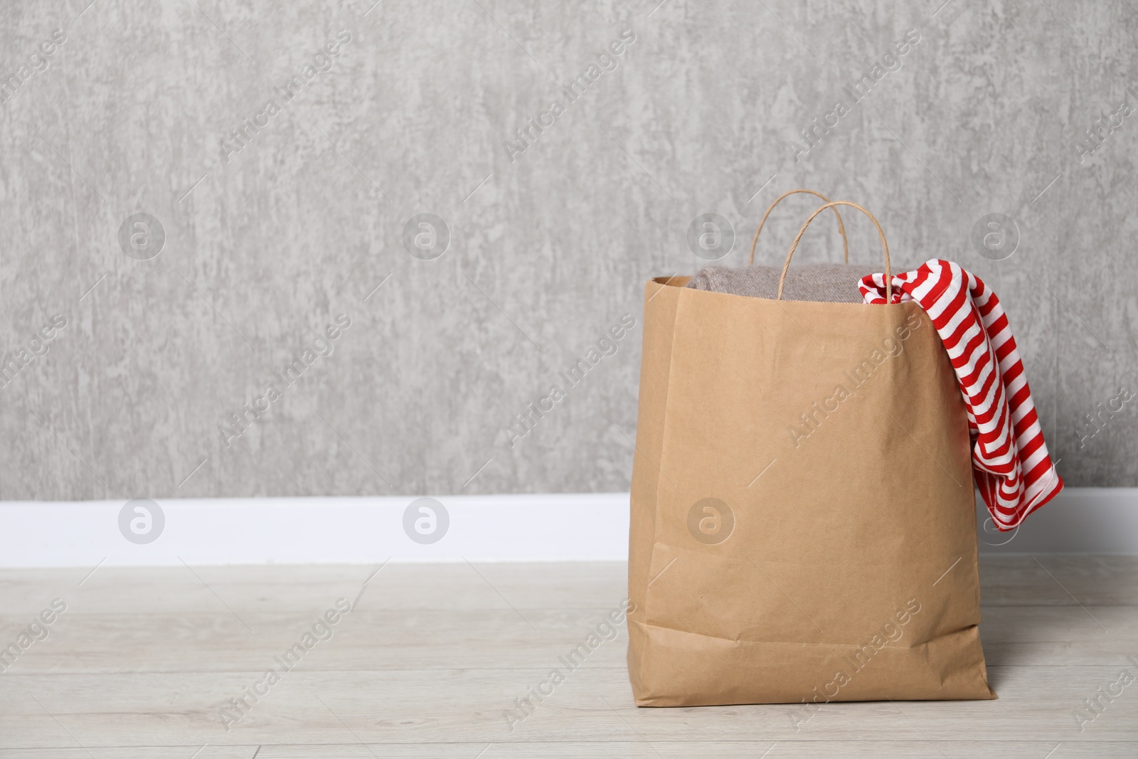 Photo of Used clothes in paper bag on floor near grey wall. Space for text