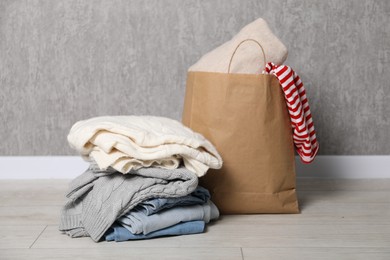 Photo of Stack of used clothes and paper bag on floor near grey wall