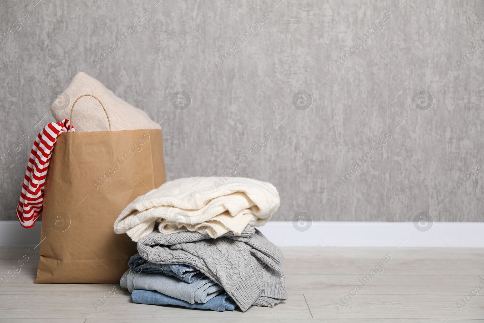 Photo of Stack of used clothes and paper bag on floor near grey wall. Space for text