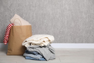 Photo of Stack of used clothes and paper bag on floor near grey wall. Space for text