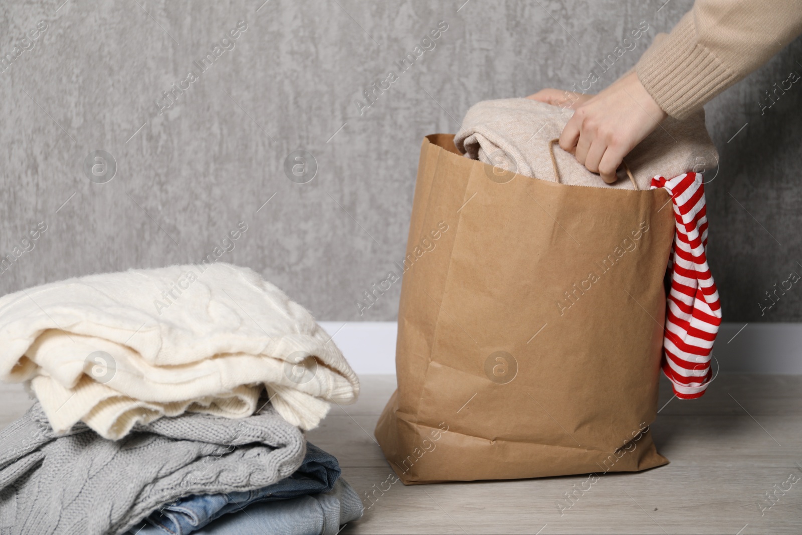 Photo of Woman with used clothes on floor near grey wall, closeup