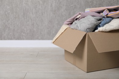 Photo of Used clothes in cardboard box on floor near grey wall. Space for text