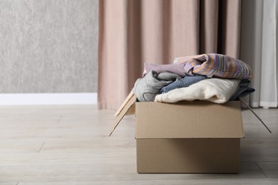 Photo of Used clothes in cardboard box on floor indoors. Space for text