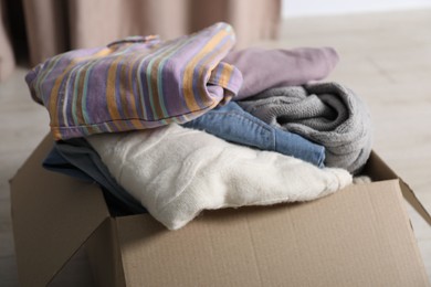 Photo of Used clothes in cardboard box on floor indoors, closeup