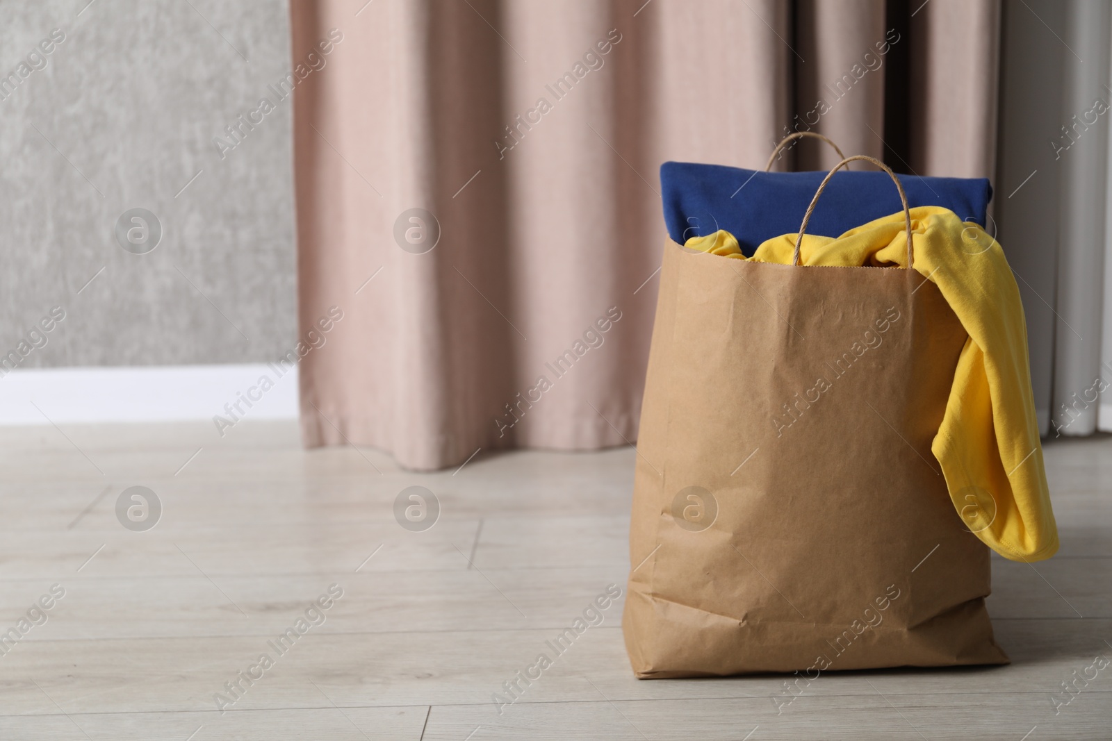 Photo of Used clothes in paper bag on floor indoors. Space for text