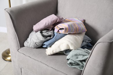 Photo of Pile of different used clothes on armchair indoors