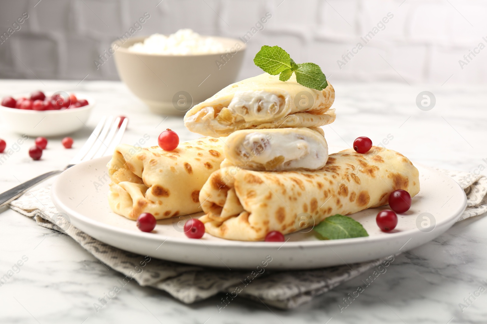 Photo of Delicious rolled crepes with cottage cheese, raisins, cranberries and mint on white marble table, closeup