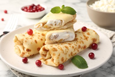 Photo of Delicious rolled crepes with cottage cheese, raisins, cranberries and mint on white marble table, closeup