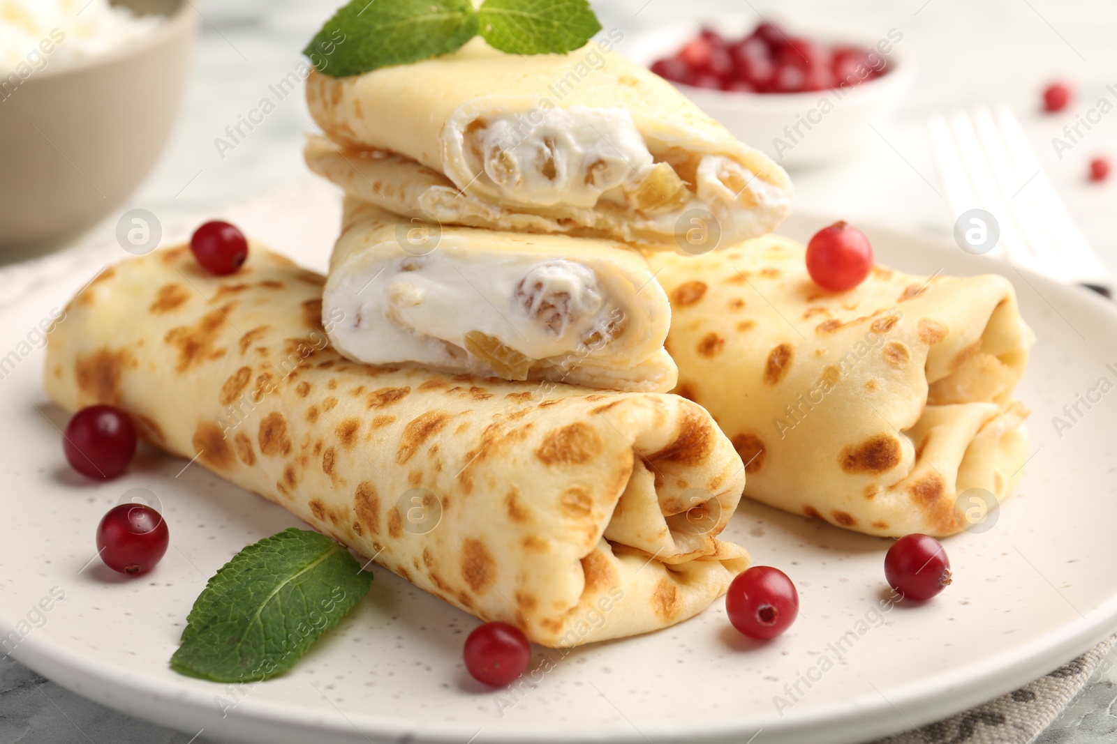 Photo of Delicious rolled crepes with cottage cheese, raisins, cranberries and mint on table, closeup