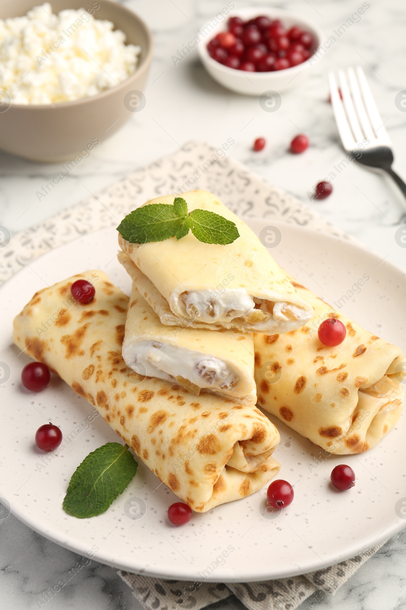 Photo of Delicious rolled crepes with cottage cheese, raisins, cranberries and mint on white marble table, closeup