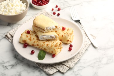 Photo of Delicious rolled crepes with cottage cheese, raisins, cranberries and mint on white marble table