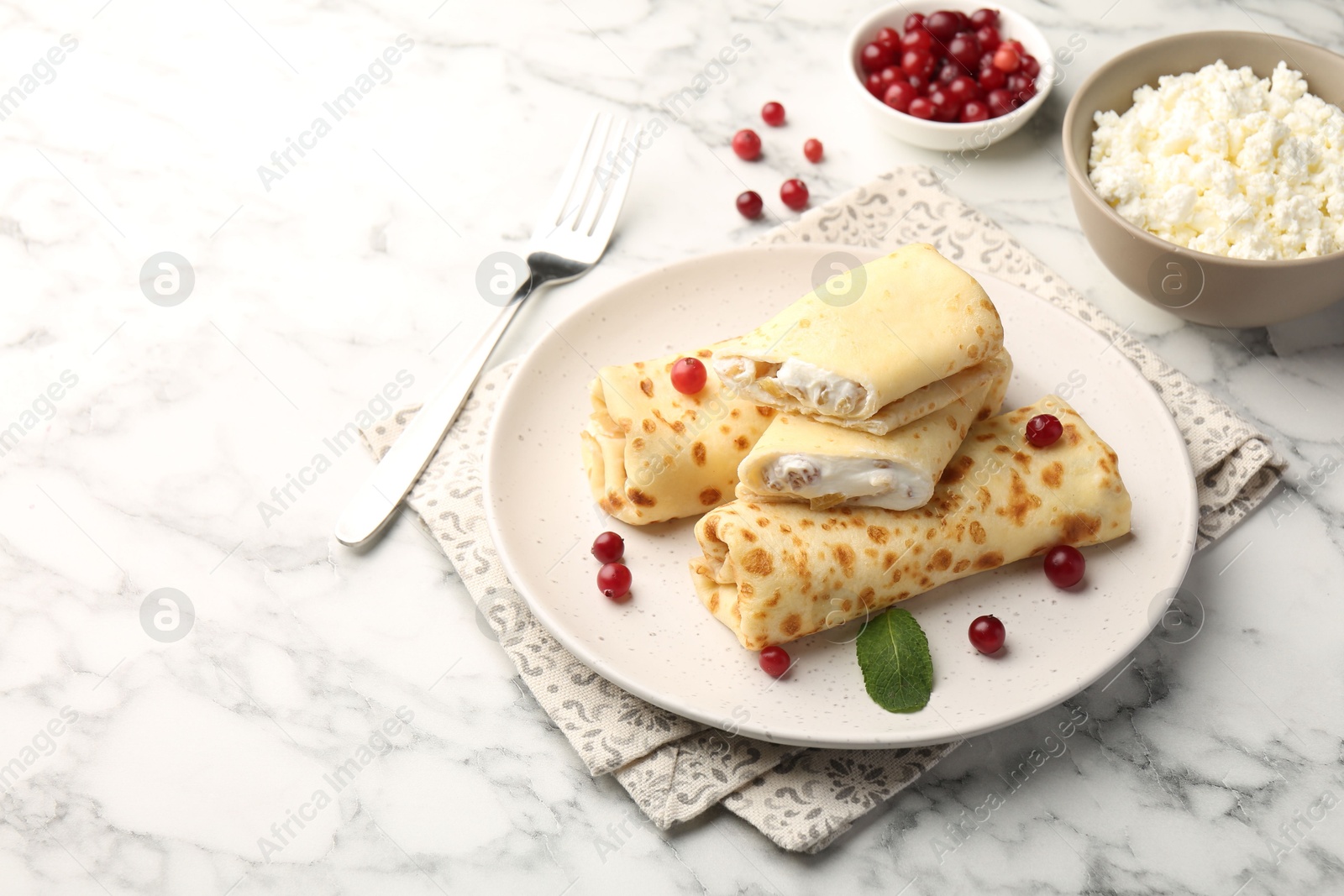 Photo of Delicious rolled crepes with cottage cheese, raisins, cranberries and mint on white marble table, space for text