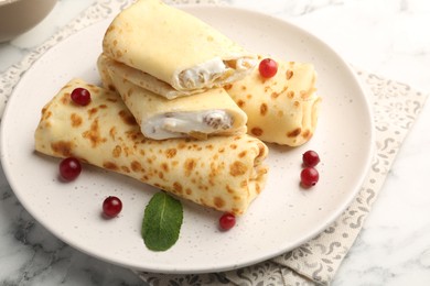 Photo of Delicious rolled crepes with cottage cheese, raisins, cranberries and mint on white marble table, closeup