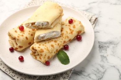 Photo of Delicious rolled crepes with cottage cheese, raisins, cranberries and mint on white marble table, closeup