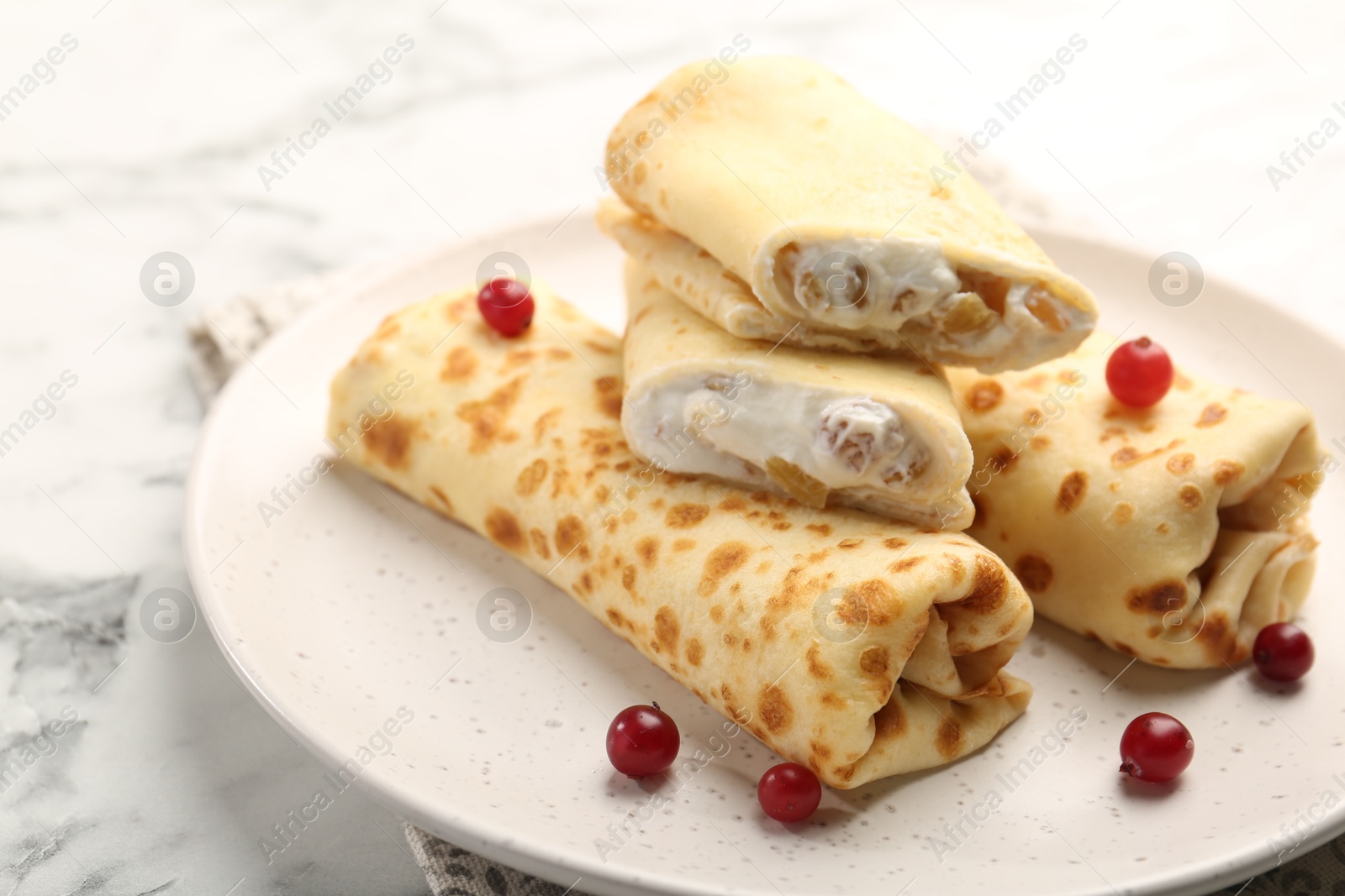 Photo of Delicious rolled crepes with cottage cheese, raisins and cranberries on white marble table, closeup