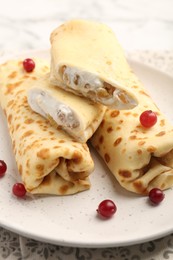 Photo of Delicious rolled crepes with cottage cheese, raisins and cranberries on table, closeup