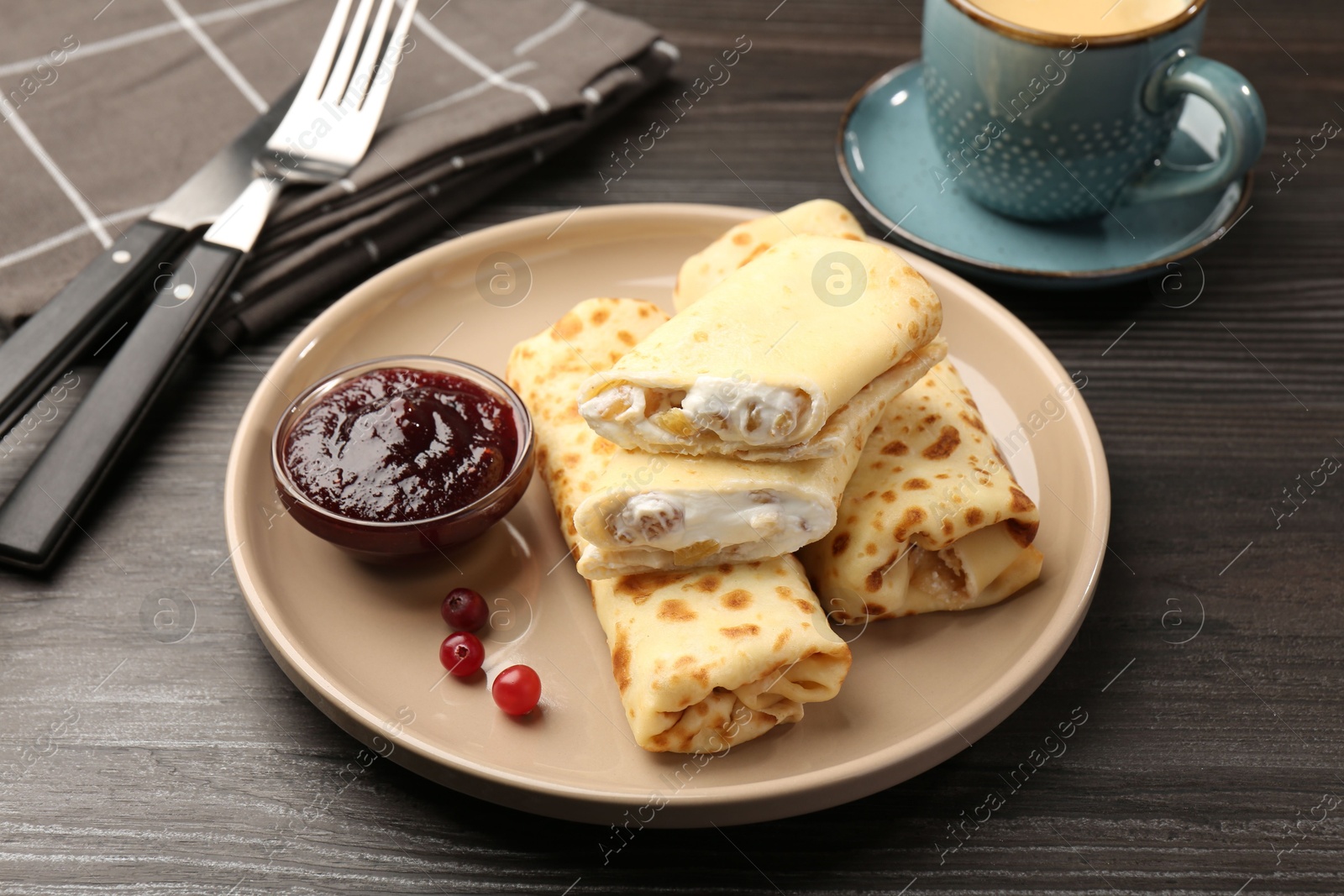 Photo of Delicious rolled crepes with cottage cheese, raisins, jam, cranberries and coffee on wooden table, closeup