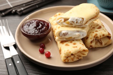 Photo of Delicious rolled crepes with cottage cheese, raisins, jam and cranberries on wooden table, closeup