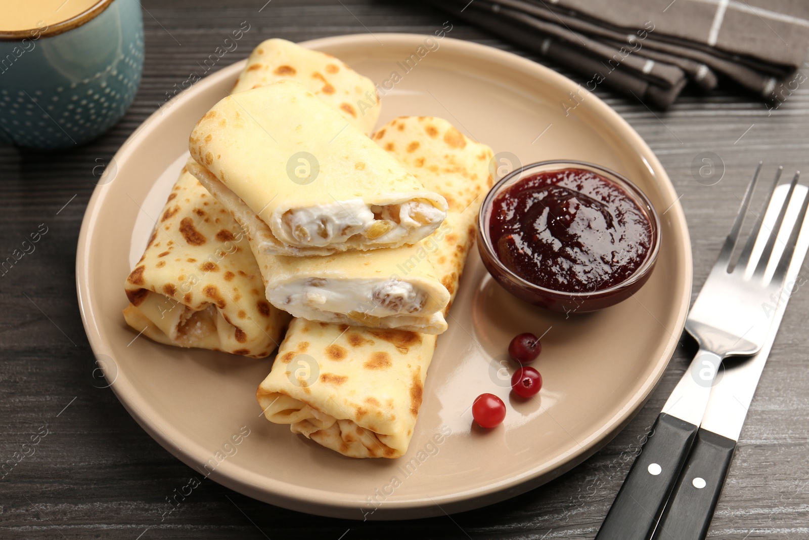 Photo of Delicious rolled crepes with cottage cheese, raisins, jam and cranberries on wooden table, closeup