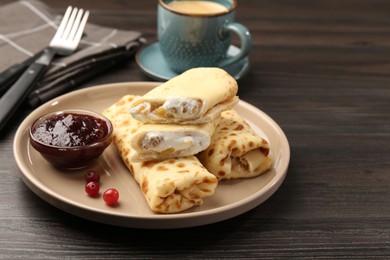 Photo of Delicious rolled crepes with cottage cheese, raisins, jam, cranberries and coffee on wooden table, closeup