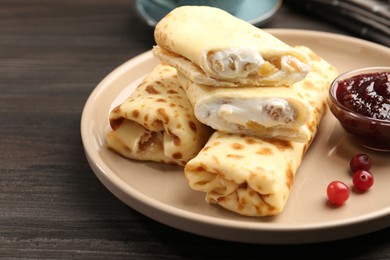 Photo of Delicious rolled crepes with cottage cheese, raisins, jam and cranberries on wooden table, closeup