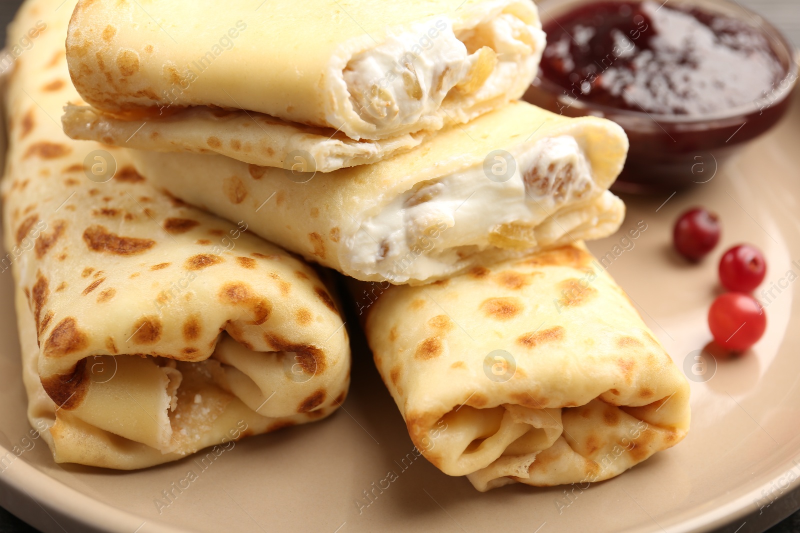 Photo of Delicious rolled crepes with cottage cheese, raisins, jam and cranberries on plate, closeup