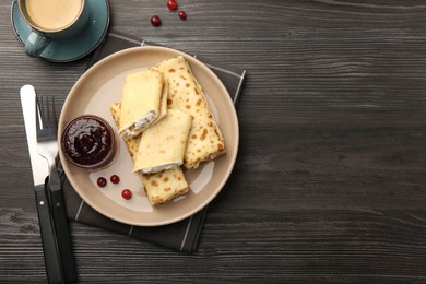 Photo of Delicious rolled crepes with cottage cheese, raisins, jam, cranberries and coffee on wooden table, flat lay. Space for text