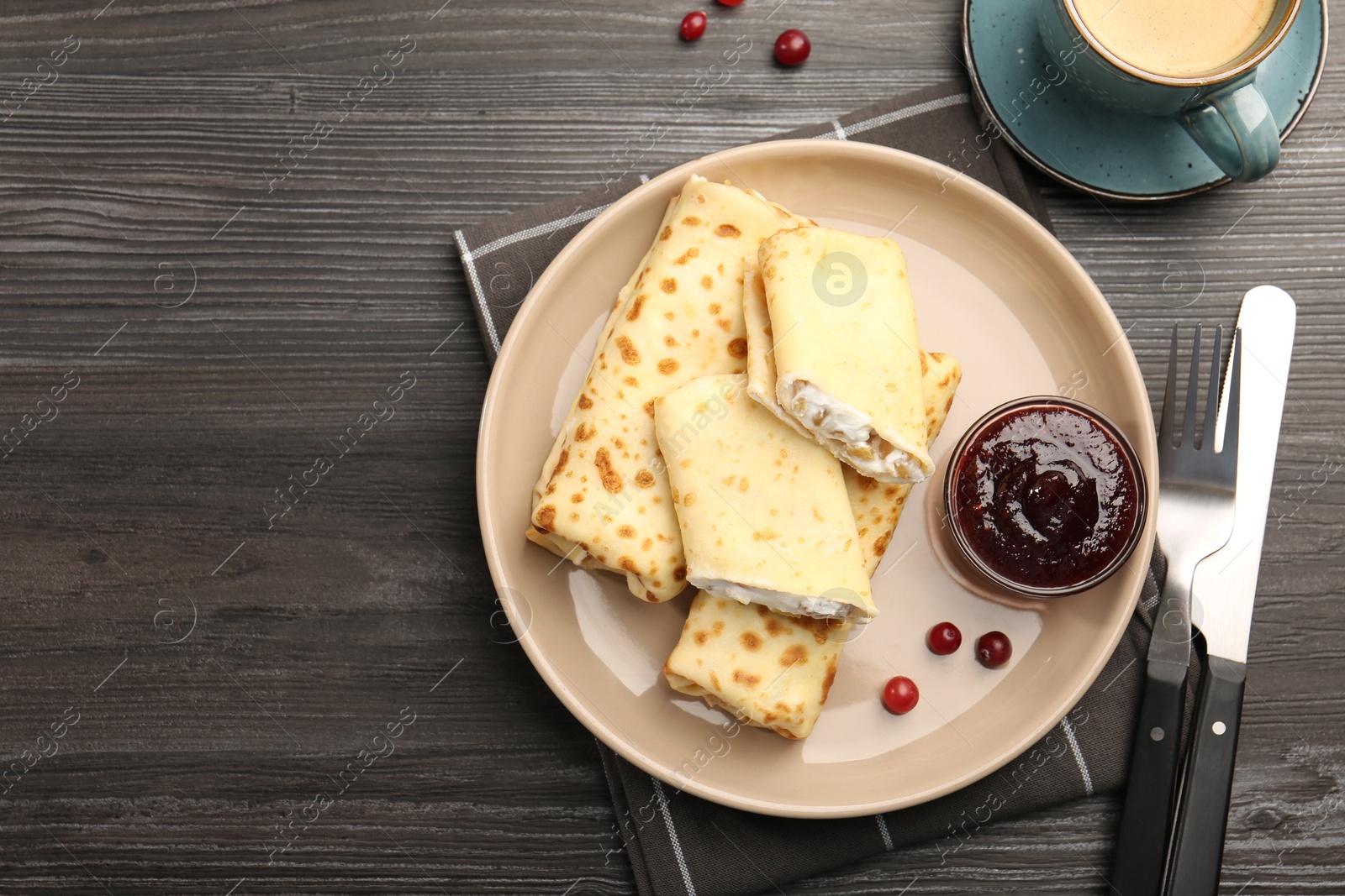 Photo of Delicious rolled crepes with cottage cheese, raisins, jam, cranberries and coffee on wooden table, flat lay. Space for text