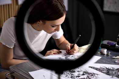 Photo of Tattoo artist drawing sketch at table with supplies in salon