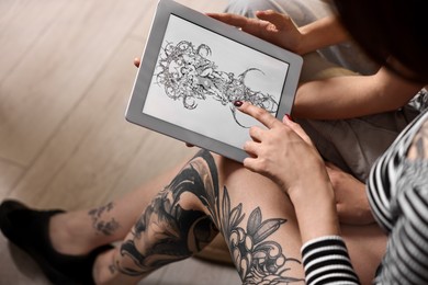 Photo of Tattoo artist showing tablet with sketch to client in salon, closeup